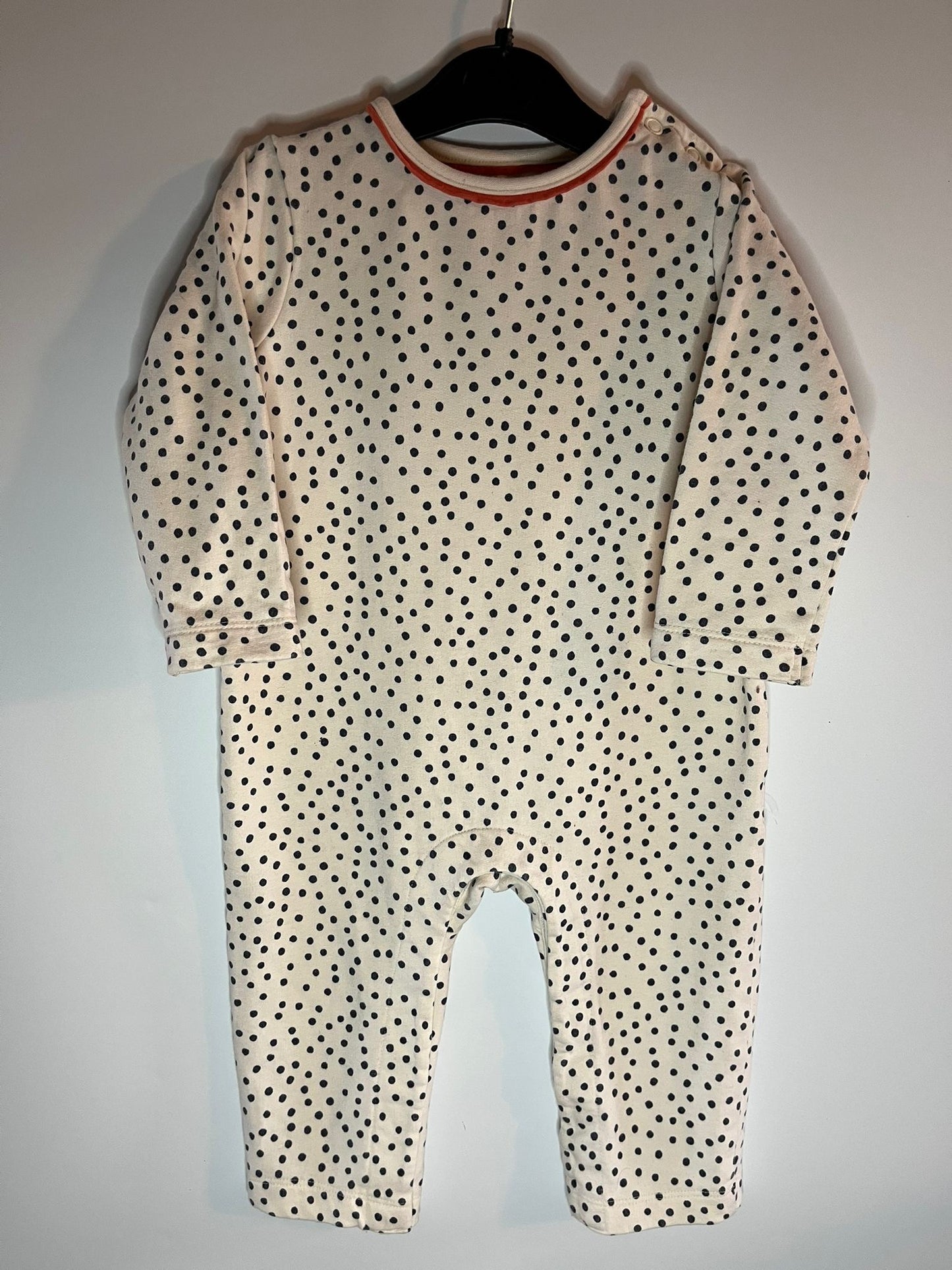 Baby onesie with black polka dots on a hanger against a white background. Preloved little drums - John Lewis size 9-12 months