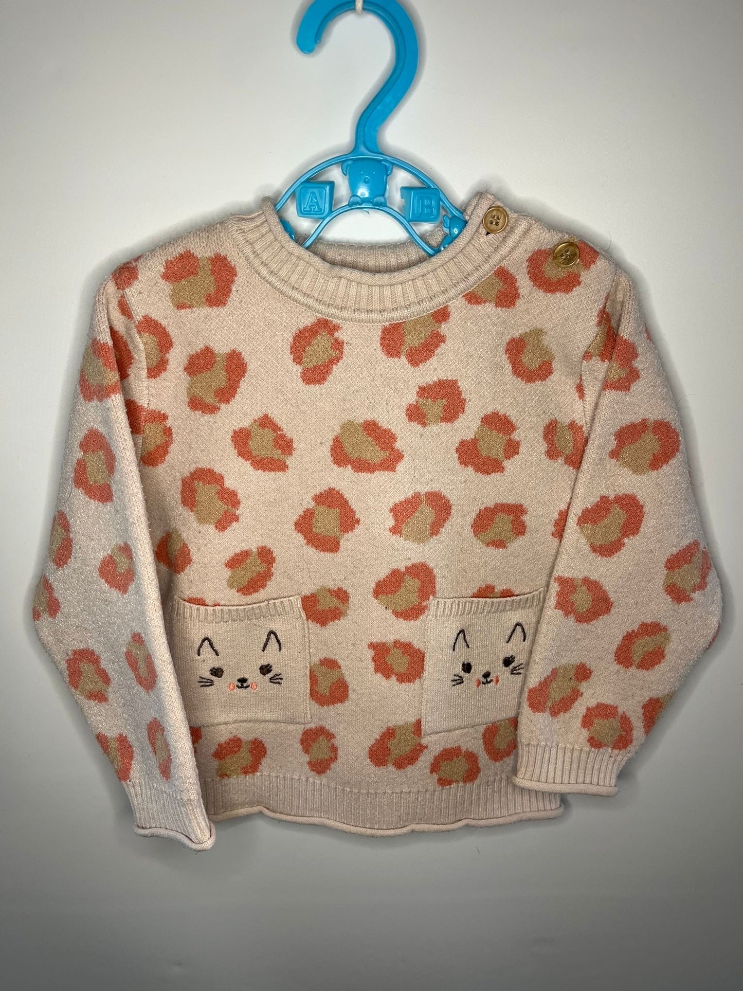 Children's sweater with cat pattern on a hanger against a plain background little drums preloved