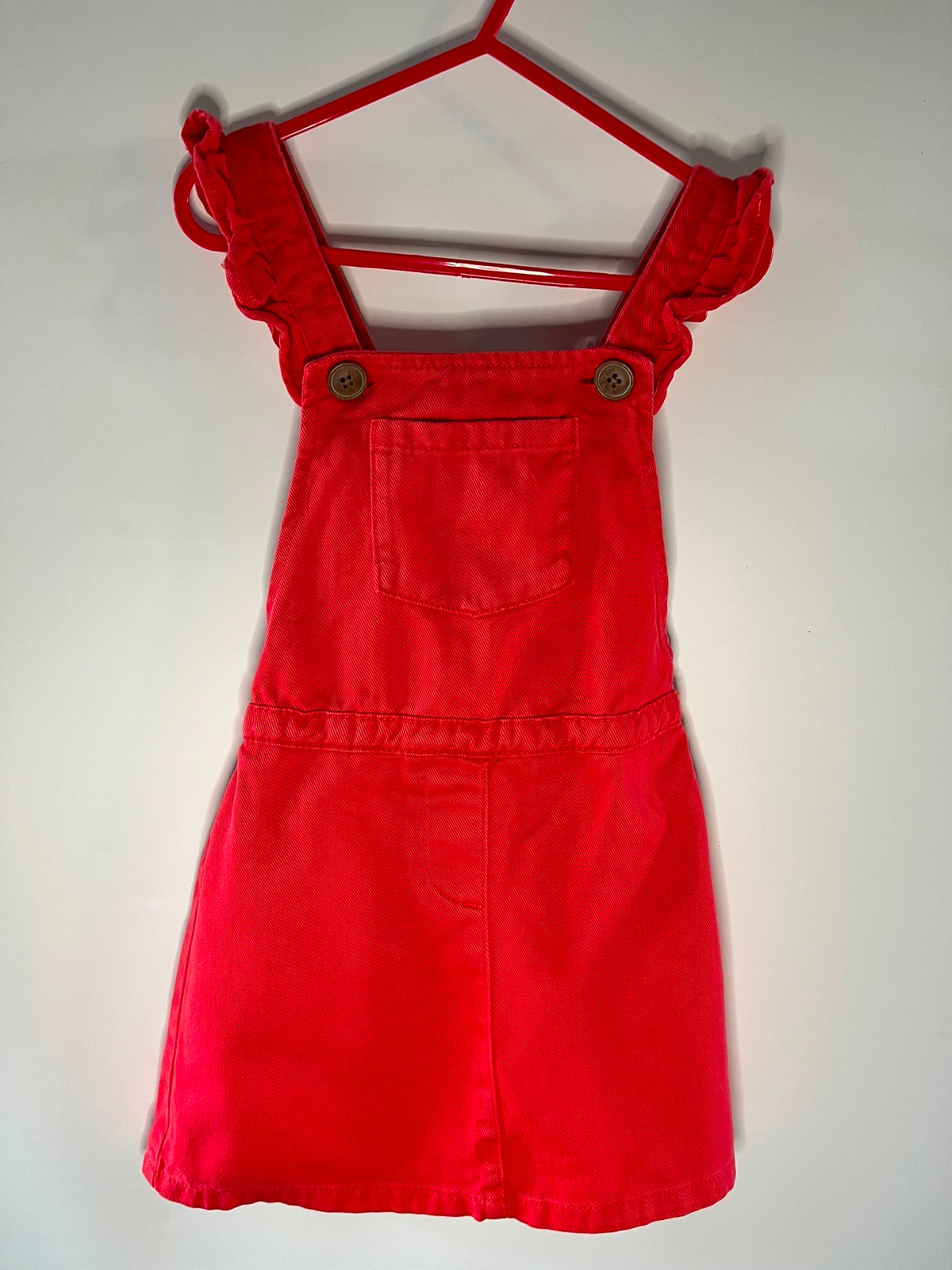 A bright red children's overall dress with ruffled shoulder straps and two front buttons, next size 3-4 preloved little drums