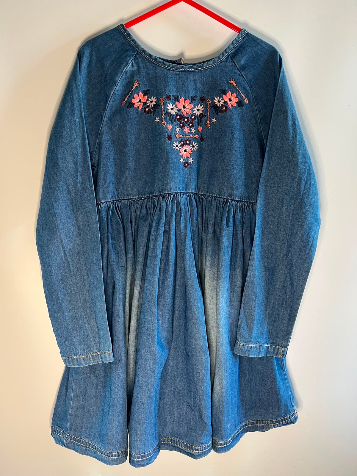 A blue denim long-sleeve dress with a gathered waist and colorful floral embroidery on the chest, mothercare preloved little drums size 6-7 years