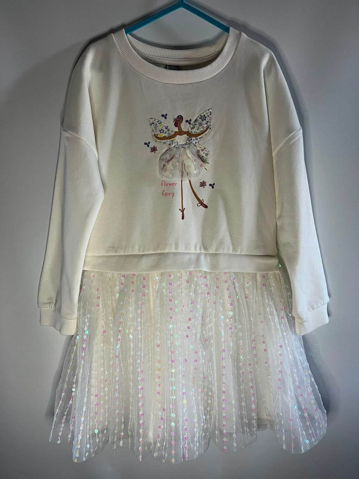 A cream-colored long-sleeve sweatshirt featuring a fairy graphic on the chest and a sheer, iridescent tulle skirt hem, TU size 5-6 years preloved little drums