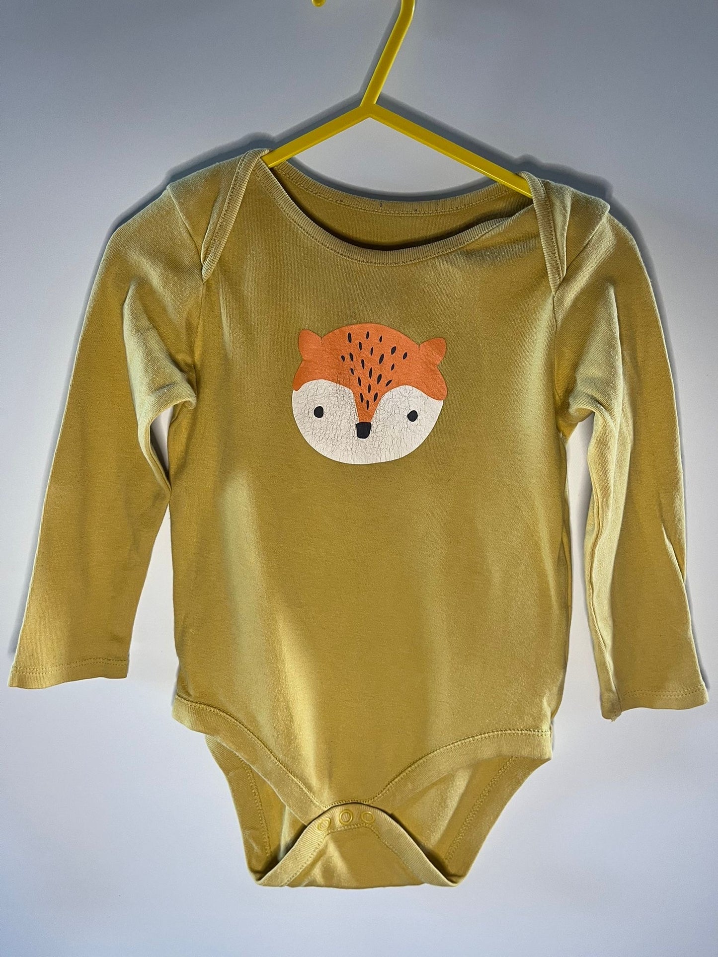 Yellow baby onesie with a fox face design on a hanger against a gray background