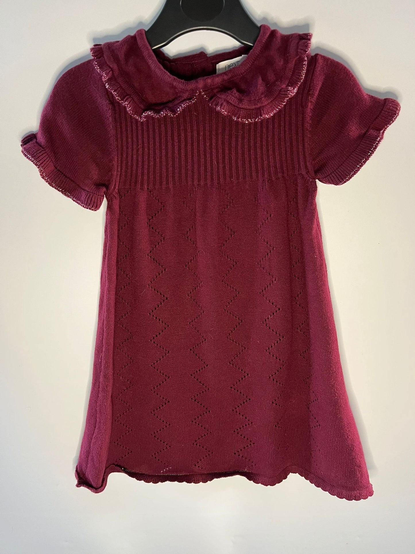 Maroon knitted dress with ruffled collar on a hanger against a white background