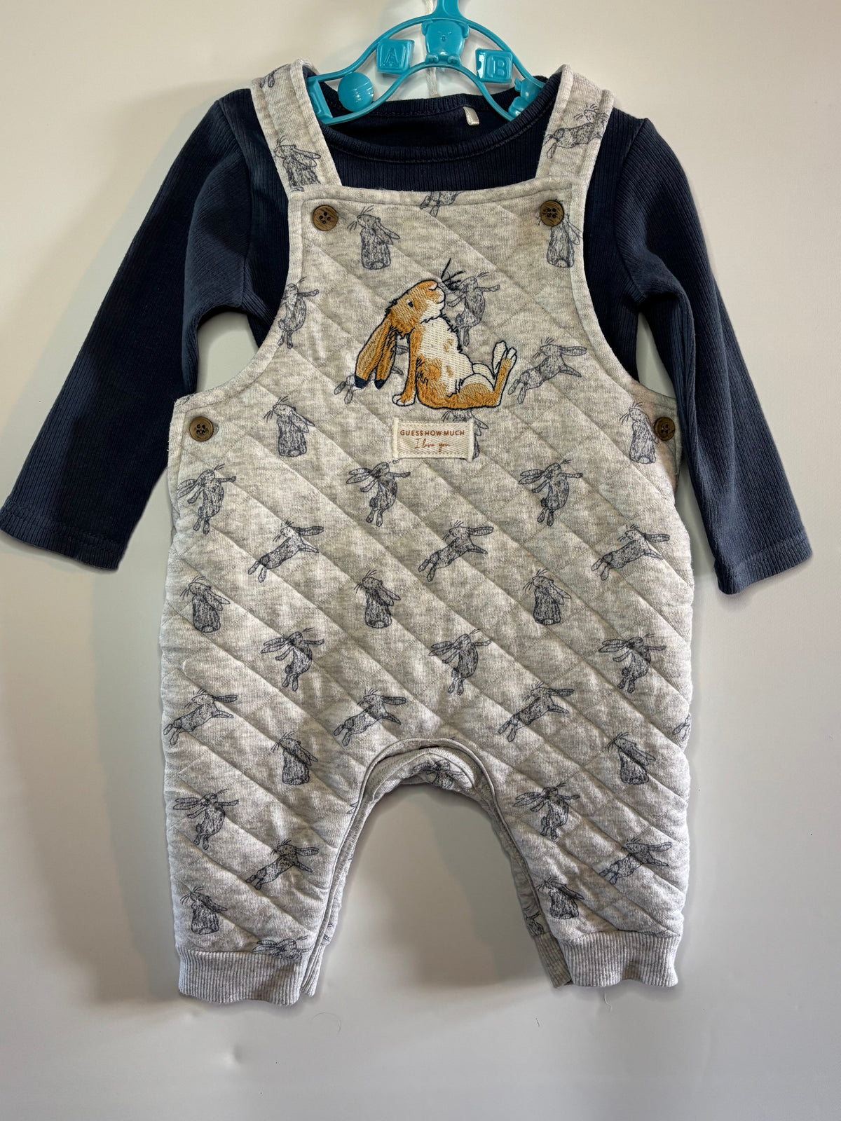A baby quilted overall romper with a gray and white bunny pattern, worn over a navy blue long-sleeve shirt tu preloved little drums 