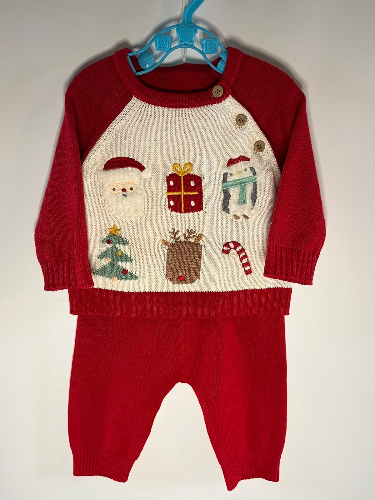 A baby holiday knit two-piece outfit consisting of a red and cream raglan sweater with Christmas-themed embroidered motifs and matching red pants, nutmeg little drums preloved 