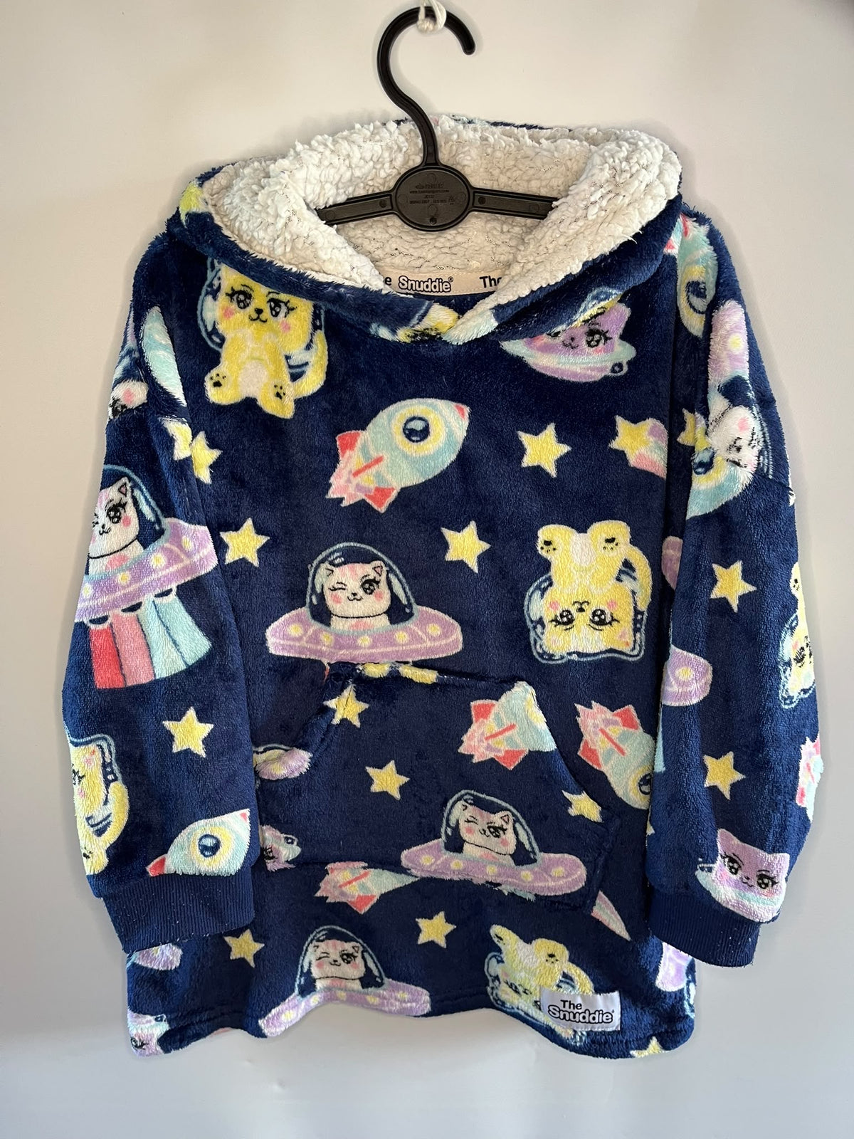 A navy blue fleece hooded sweatshirt with a white sherpa lining, featuring a colorful cartoon space print with cats in space suits, rockets, and stars, hanging on a black hanger against a plain light background.