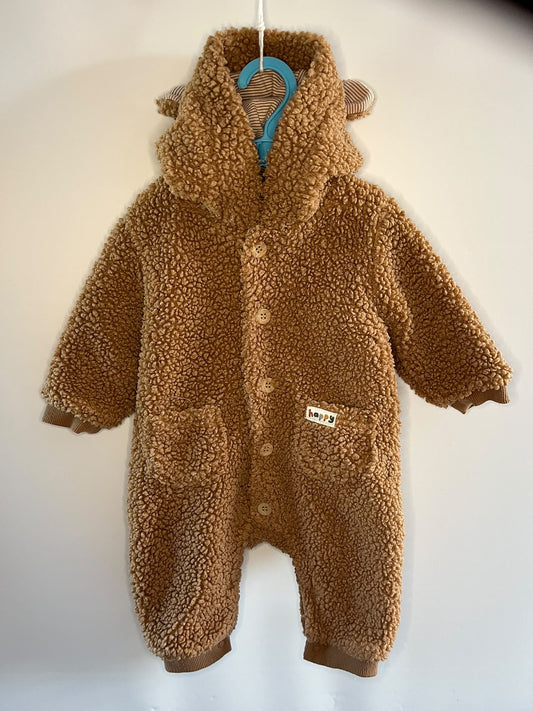 A baby's brown sherpa fleece hooded one-piece romper with ear details on the hood, hanging on a blue hanger against a plain off-white wall.