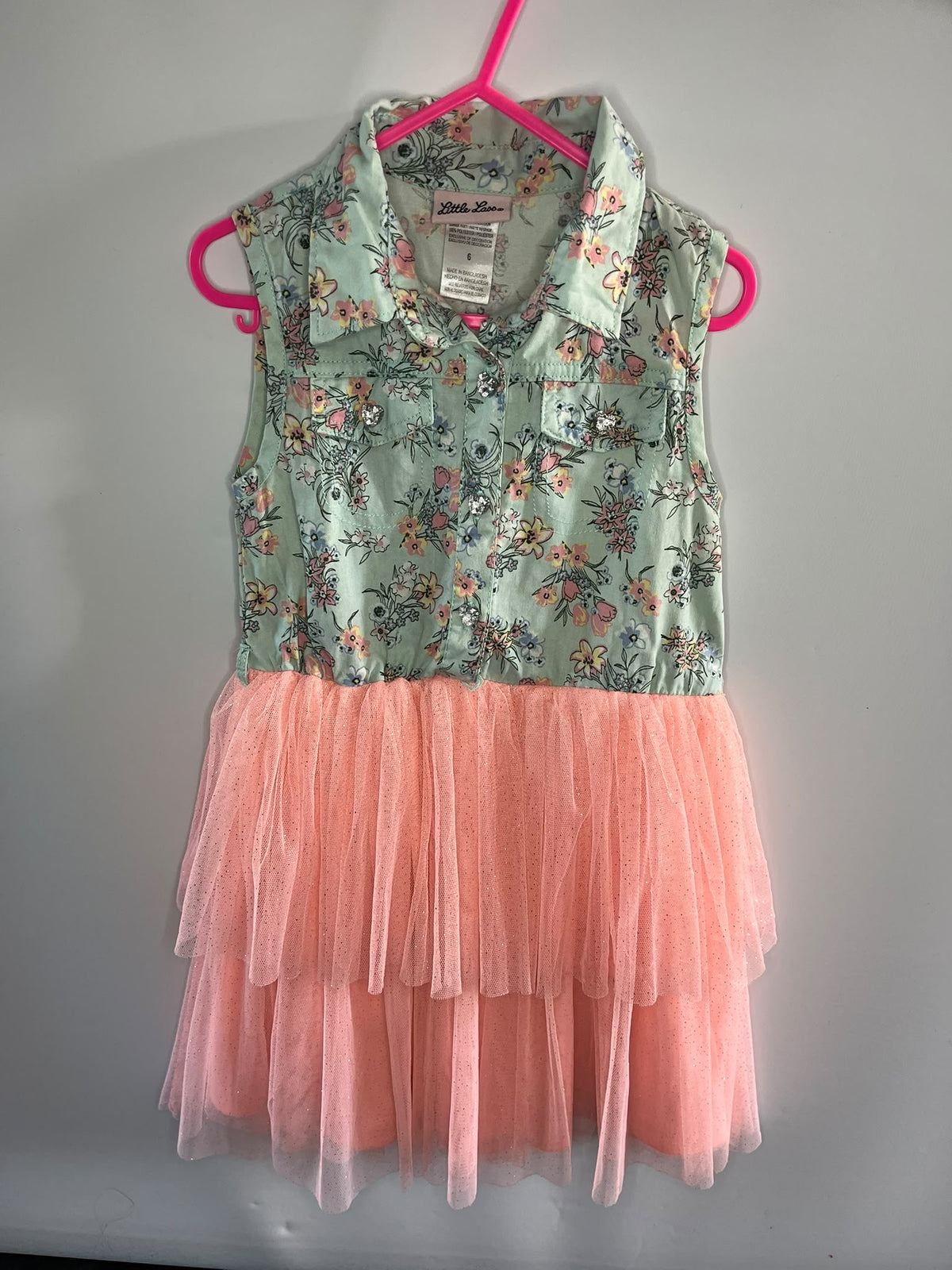 A sleeveless children's dress. The top portion has a light green floral print with pink, orange, and blue flowers, and the bottom is a layered peach-pink tulle tutu skirt.