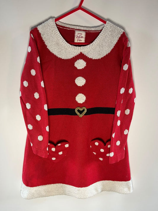 A festive red knit sweater dress with white polka dots, a fuzzy white Peter Pan collar, a black belt detail with a heart-shaped buckle, and white faux-fur trim at the collar, cuffs, and hem, hanging on a red hanger against a plain light background.