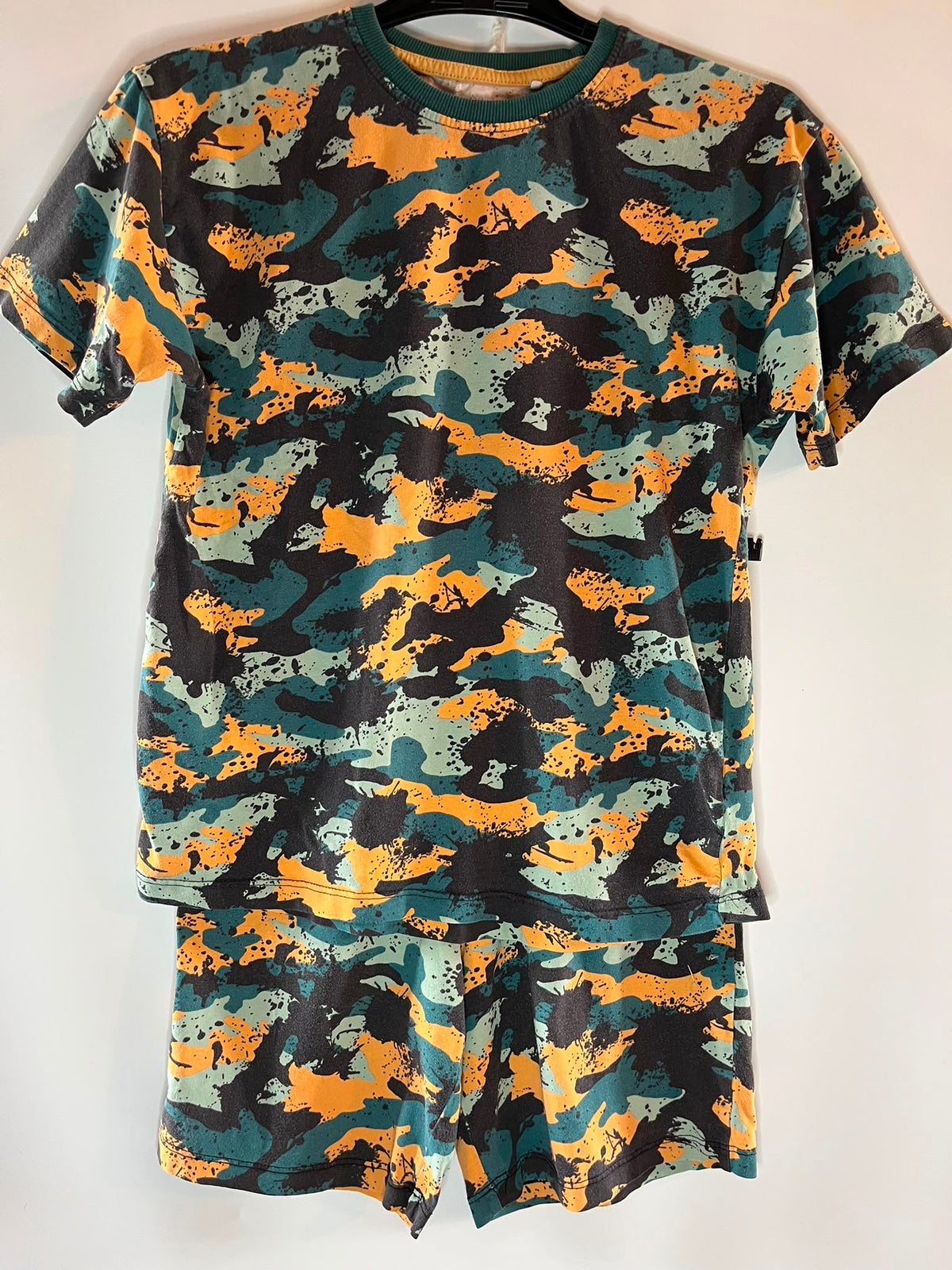 A two-piece short-sleeve pajama set consisting of a crewneck t-shirt and matching shorts, both featuring a distressed camouflage pattern in orange, teal green, black, and light gray, next size 9 years preloved little drums 