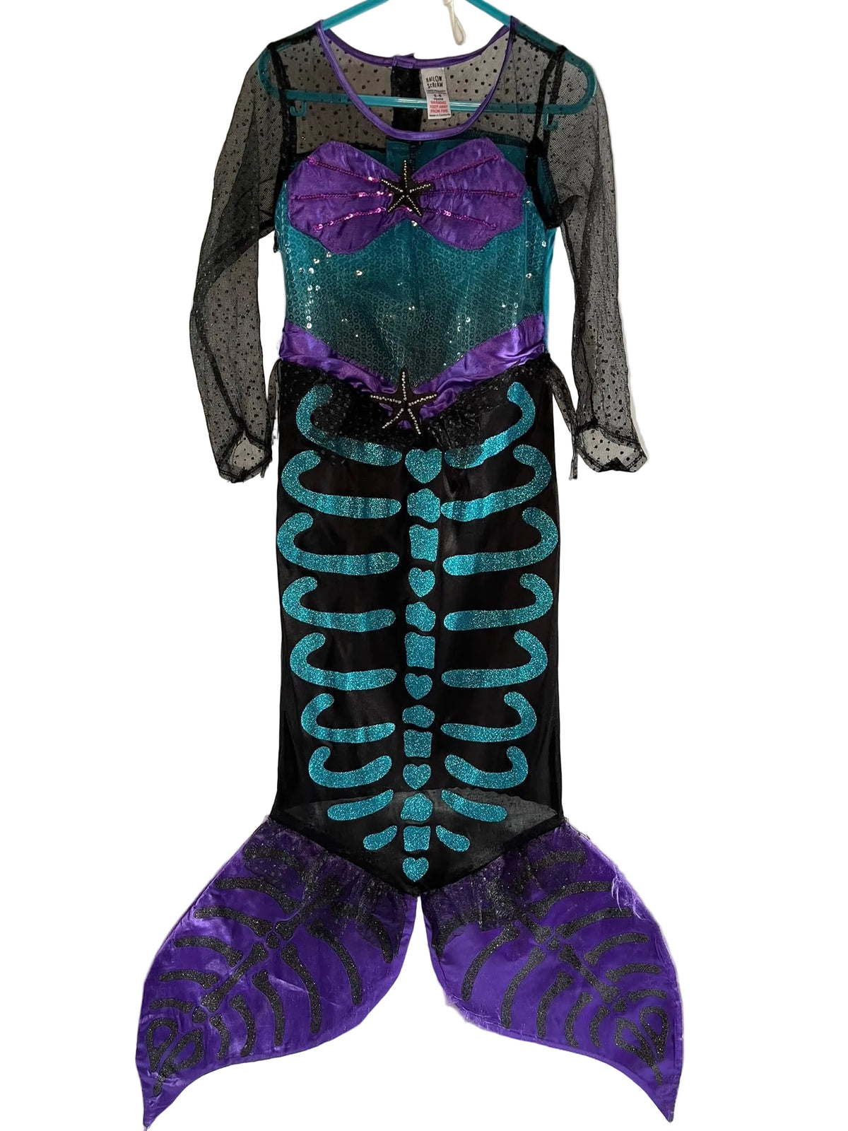 A mermaid costume dress The costume features a black mesh body with a purple sequined sweetheart bust, a teal sequined midsection, a black lower section with a teal sequined skeletal rib design, and purple patterned fin flaps at the bottom.