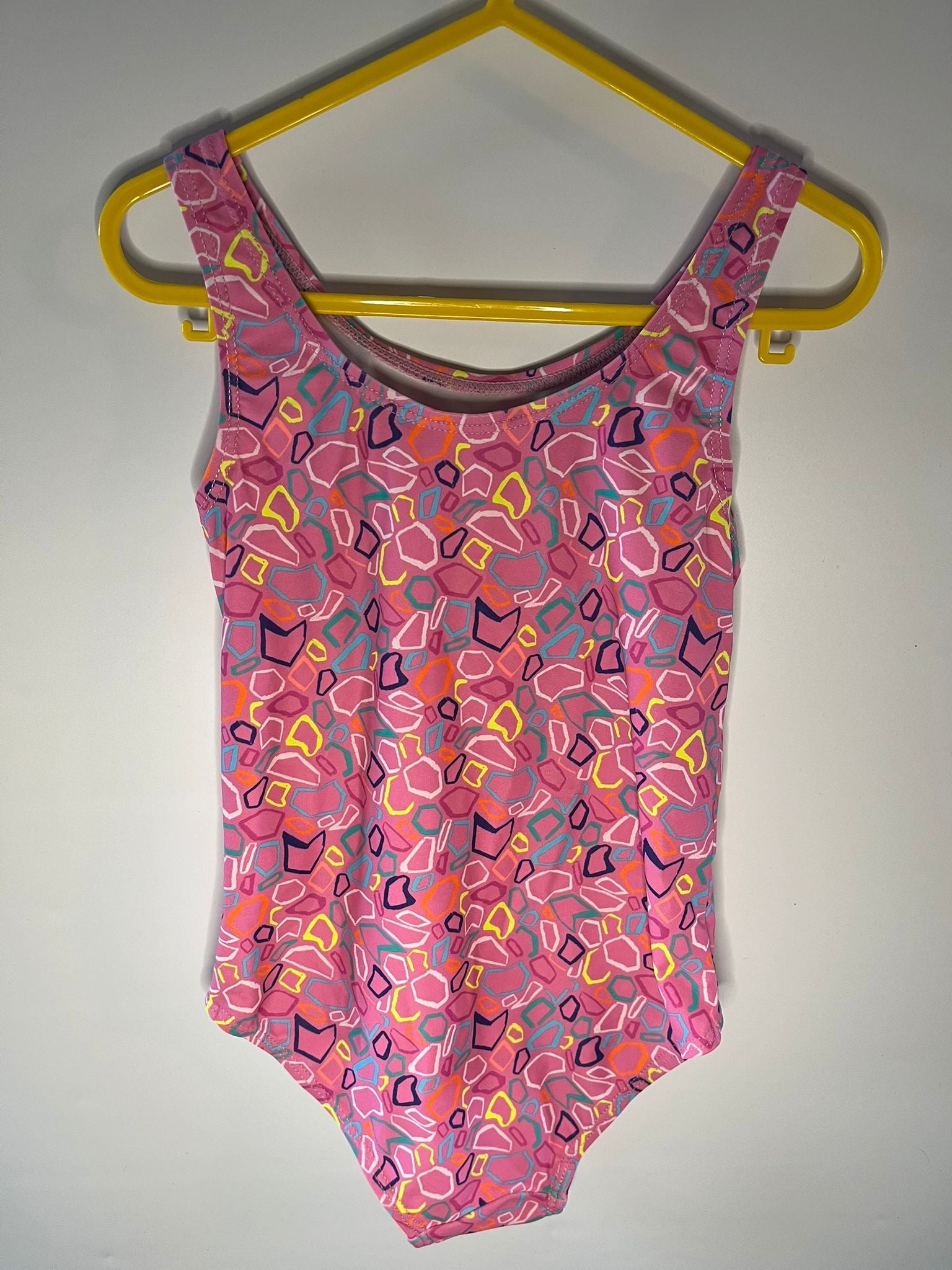 Pink swimsuit with colorful patterns on a yellow hanger against a white background preloved little drums 