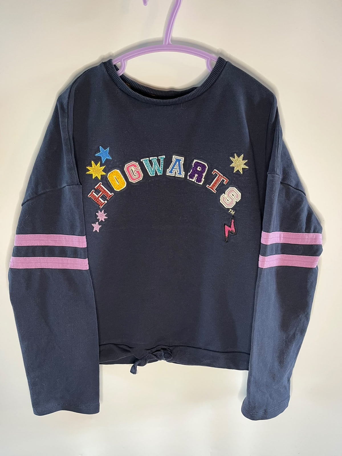 A navy blue cropped sweatshirt with 'HOGWARTS' written across the chest in colorful letters and decorated with stars, M&S preloved little drums 