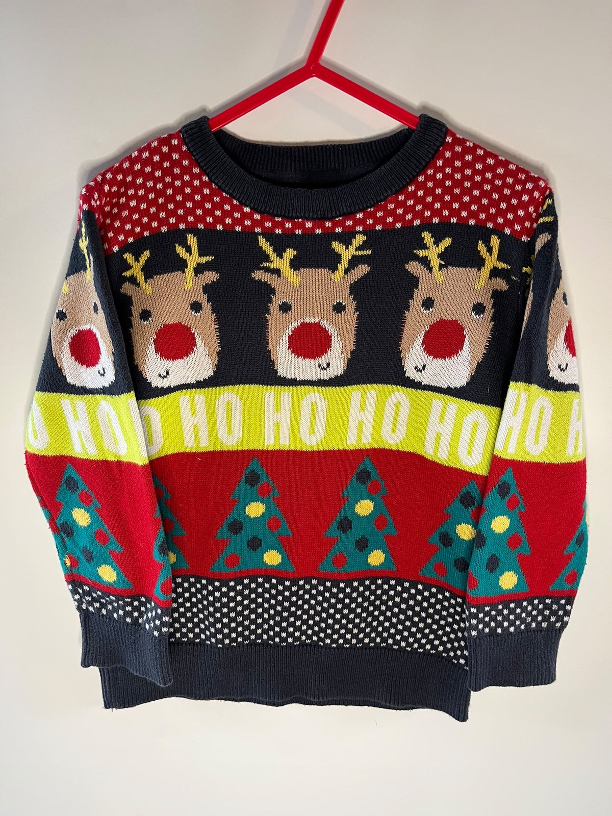 A festive Christmas sweater with a navy blue base, featuring a pattern of reindeer faces, red and white polka dots, a yellow band with 'HO HO HO' text, and green Christmas trees. Preloved F&F little drums 