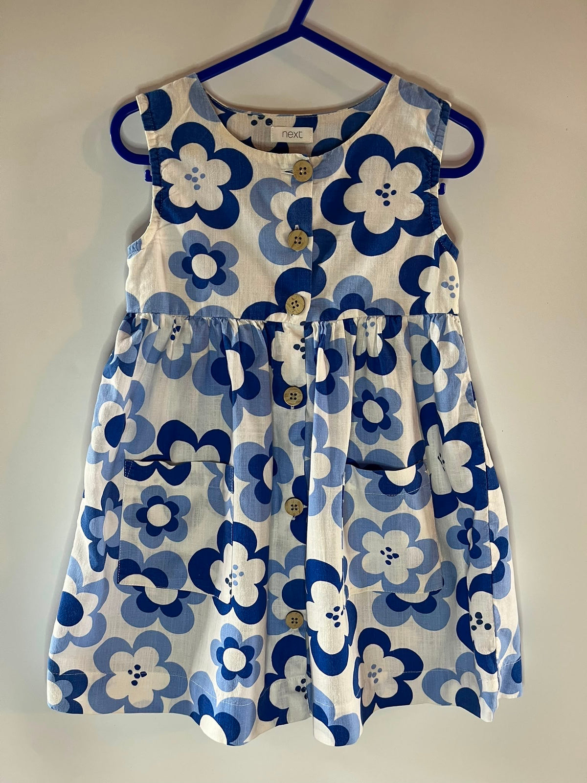 A sleeveless white dress with a bold blue and navy floral pattern, featuring a button-down front and a gathered waist, preloved little drums next size 2-3 years 