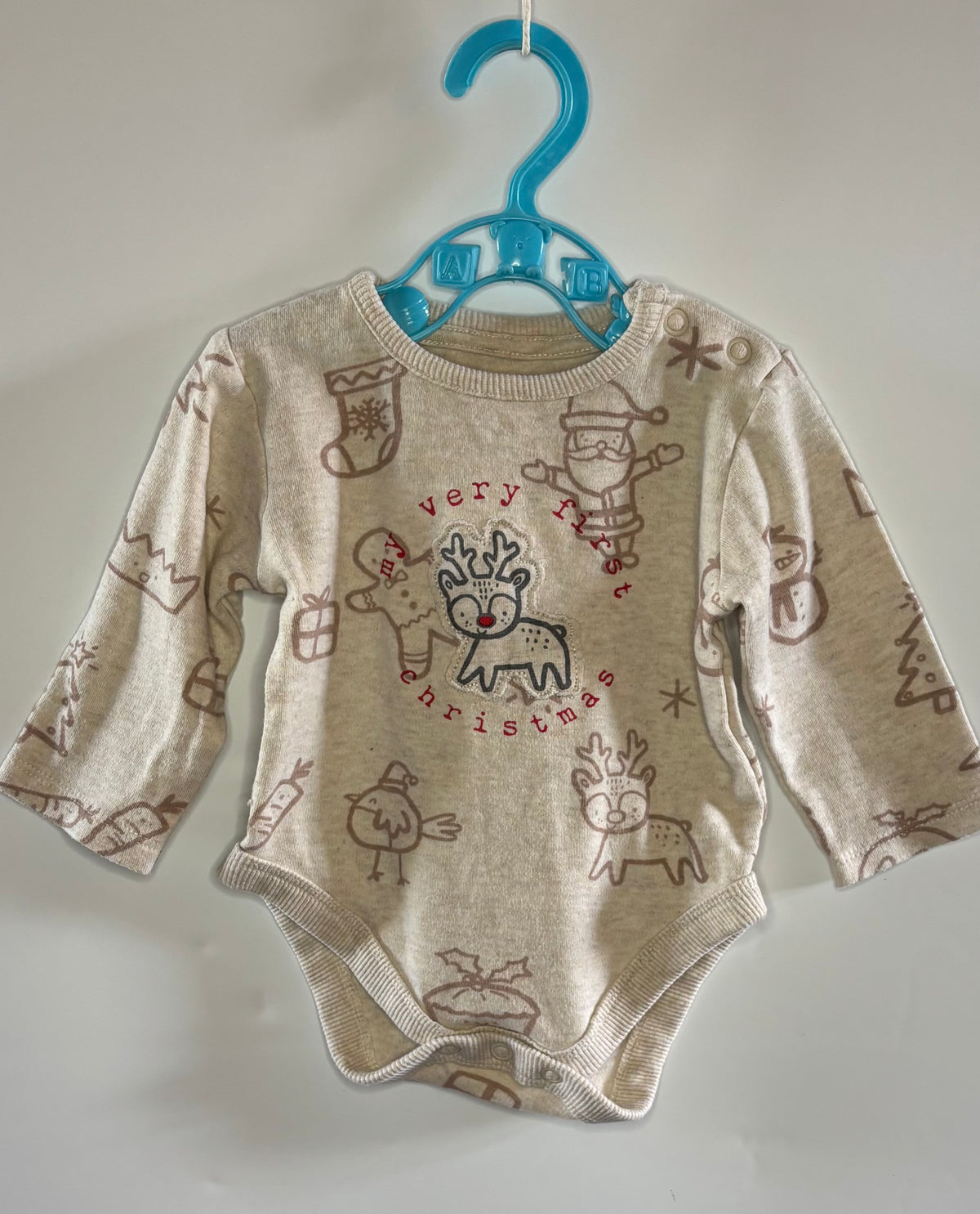 A baby long-sleeve bodysuit in cream with brown Christmas-themed illustrations and a central 'very nice Christmas' graphic, hanging on a blue plastic hanger against a plain light wall.