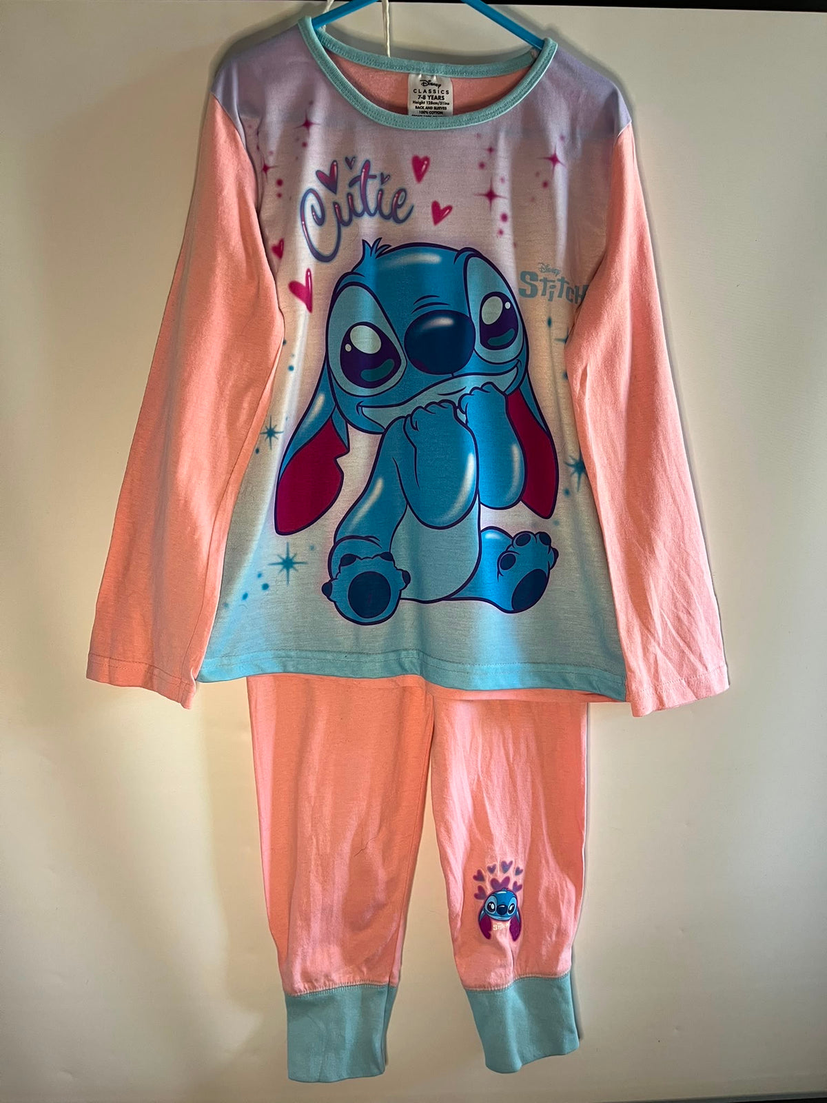 A two-piece children's pajama set featuring a long-sleeve top and matching pants in pastel pink and light blue. The top has a large graphic of the Disney character Stitch on the front, with the word 'Chillie' printed above. Preloved little drums 