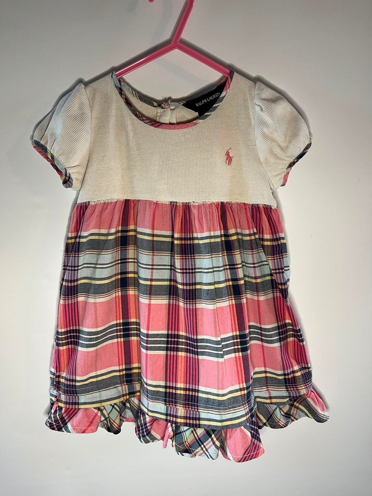 A girl's short-sleeve dress by Ralph Lauren, featuring a solid cream top half with a small embroidered polo player logo, and a pink, red, black, and yellow plaid skirt half, size 3 years preloved little drums 