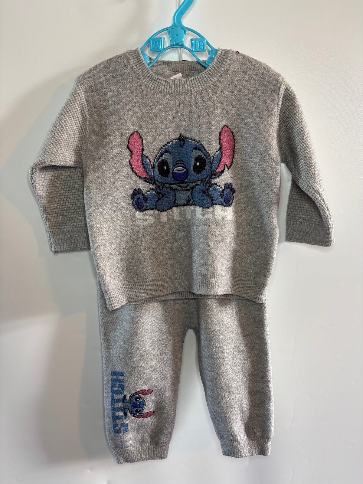 A children's two-piece knit loungewear set in heather gray, featuring a long-sleeve top with a large Stitch graphic on the chest and matching jogger pants with a vertical Stitch print. The set is displayed on a blue plastic hanger against a plain white wall.