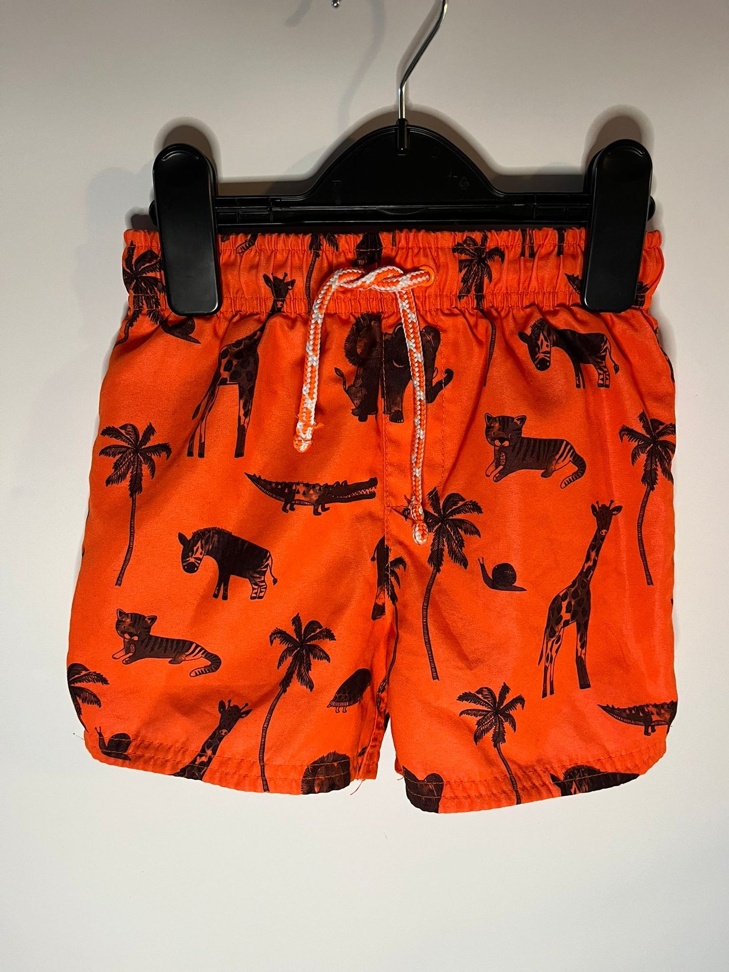 Orange shorts with black animal prints on a hanger against a white background