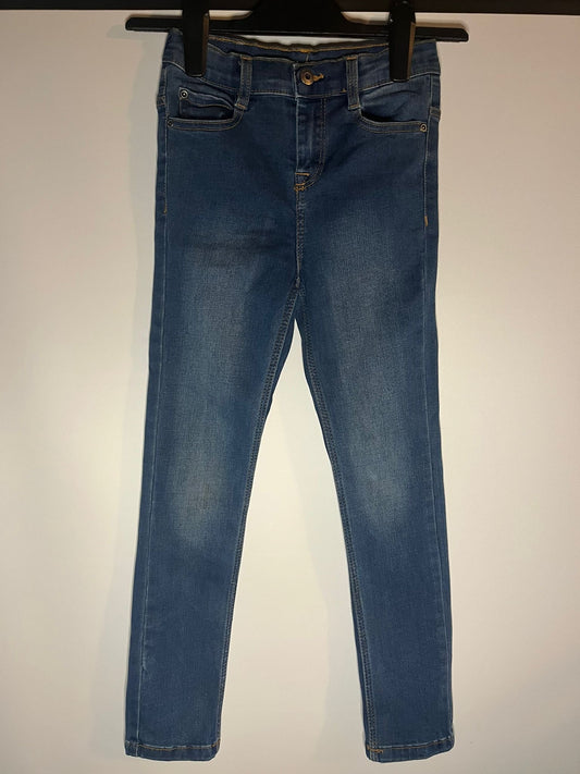 Blue jeans hanging on a hanger against a plain background