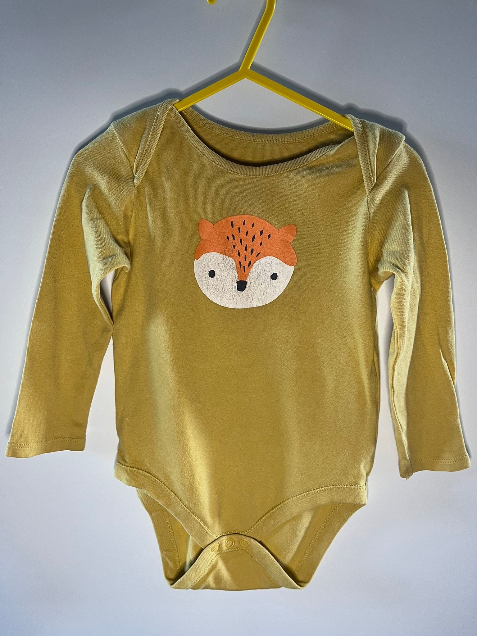Yellow baby onesie with a fox face design on a hanger against a gray background