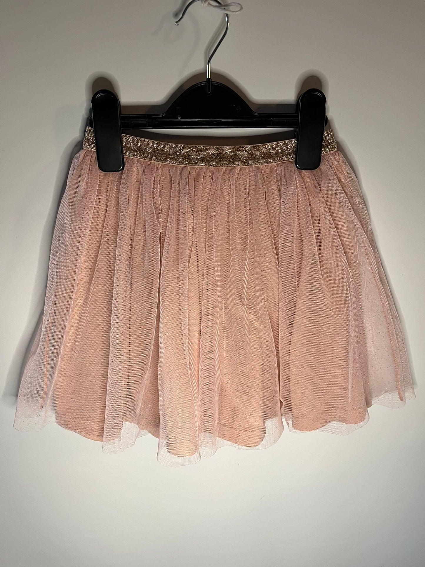 Pink tulle skirt on a hanger against a plain background