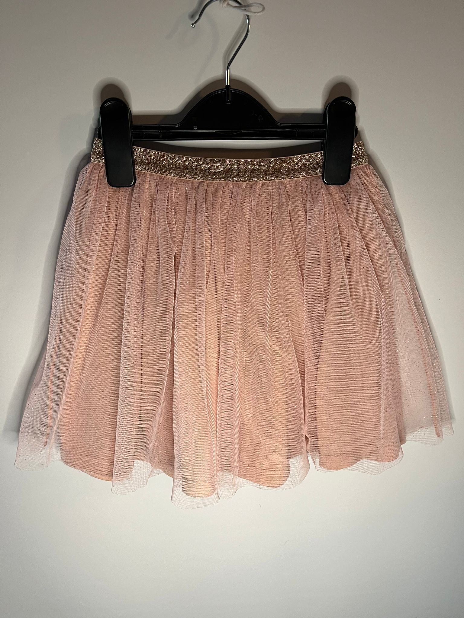 Pink tulle skirt on a hanger against a plain background