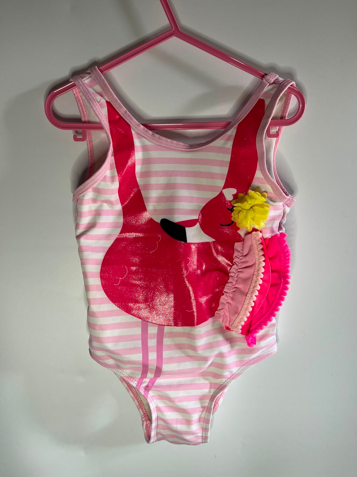 A pink and white striped girl's one-piece swimsuit with a glossy pink flamingo applique and a pink ruffled headband with a yellow pom-pom flower, TU preloved little drums 