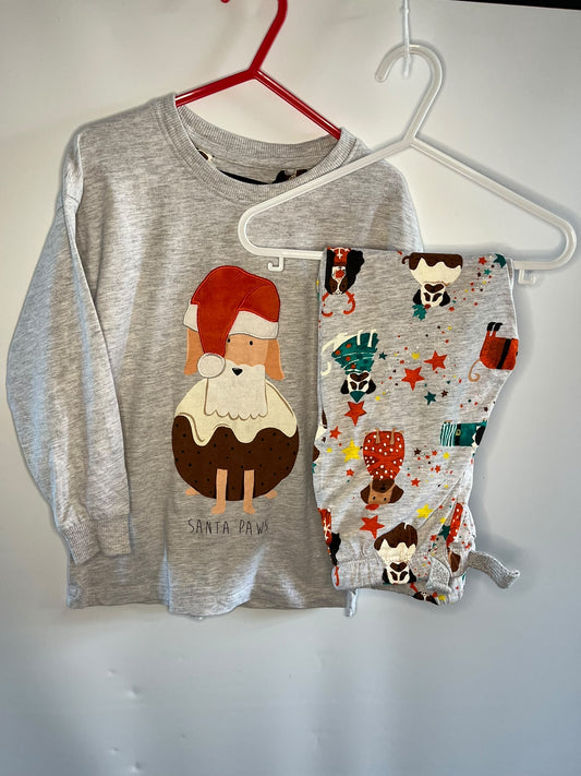 A children's two-piece holiday outfit set hanging on hangers against a plain wall. The set includes a heather gray long-sleeve shirt with a Santa Claus graphic and matching patterned shorts.