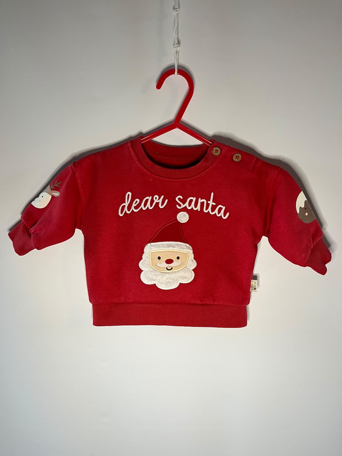 A red baby jumper features 'dear santa' embroidered in white script across the chest above a plush Santa face. Maybe baby preloved little drums 