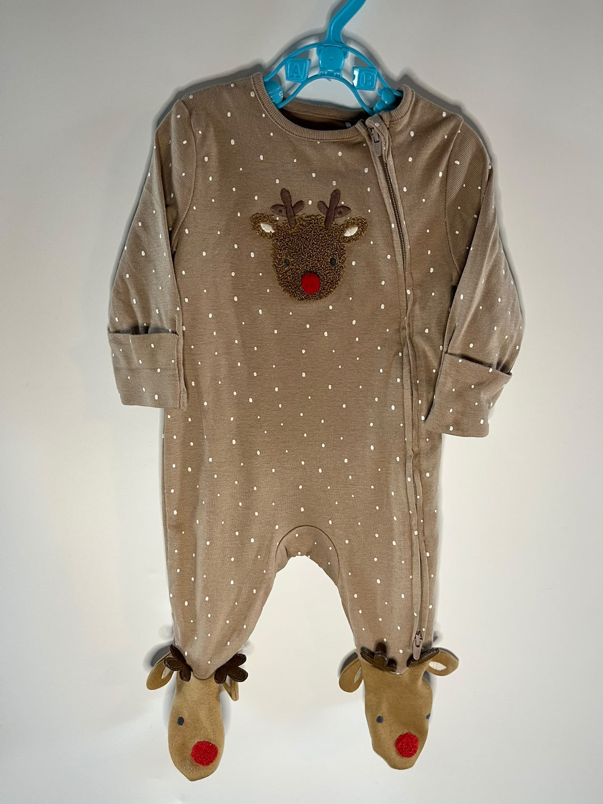 A baby footed one-piece sleeper in a warm taupe-brown color with white polka dots, featuring an applique reindeer face on the chest and matching reindeer feet with red noses, M&S preloved little drums.