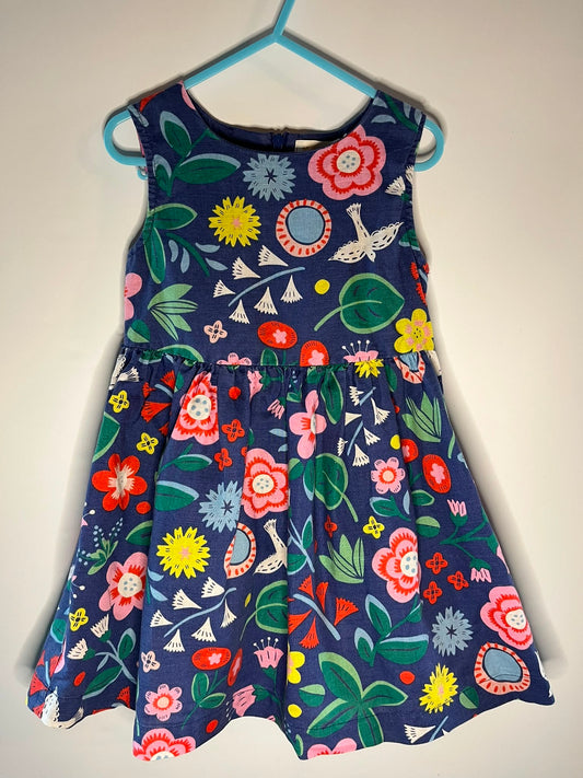 A sleeveless children's dress mini boden.  The dress has a navy blue base with a colorful floral and bird pattern in pink, red, yellow, green, and white. Size 3-4 years preloved little drums 