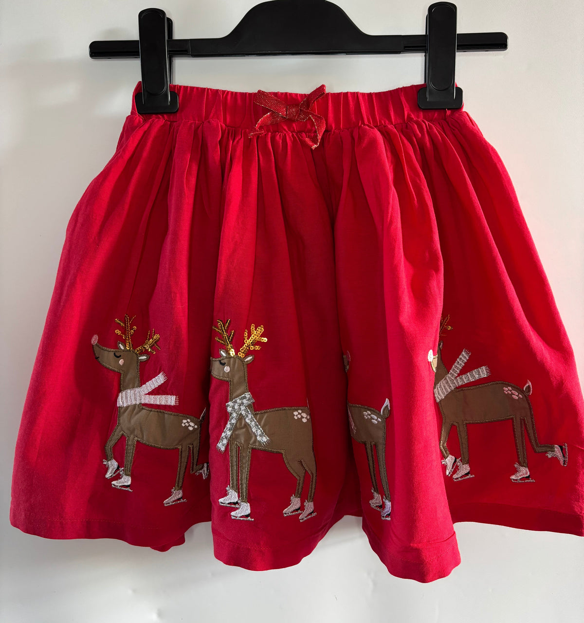 A red children's skirt with embroidered brown reindeer motifs wearing white scarves,