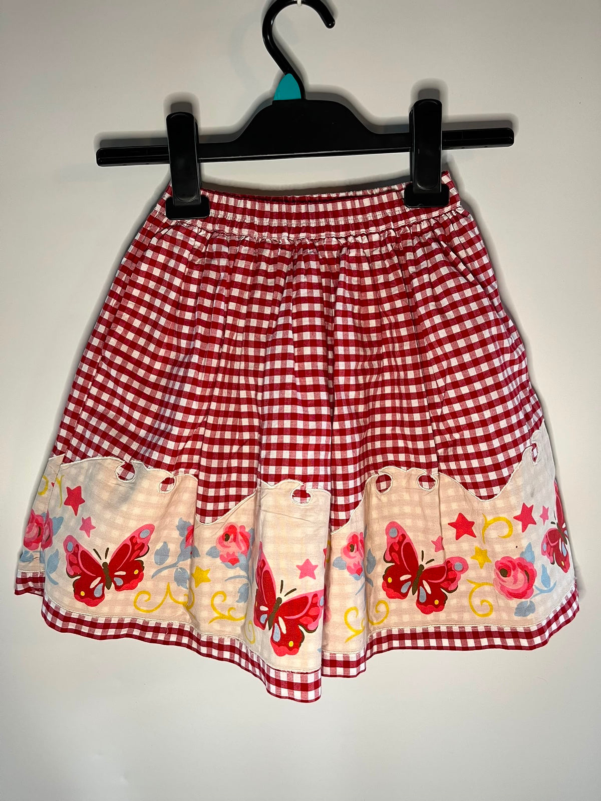 A red and white gingham skirt with a decorative ruffled hem featuring embroidered red butterflies, pink flowers, and yellow stars on a cream background, cath Kidson size 4-5 years preloved little drums 